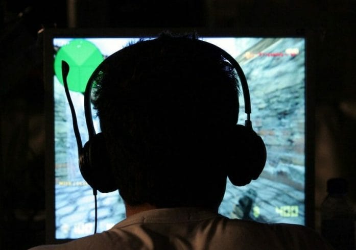 Computer gamer in headset shadowed in front of blurry screen