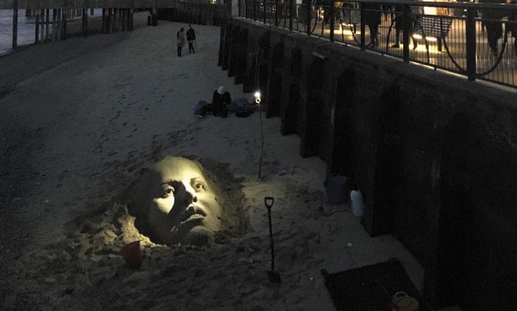 Giant face in the sand as people look on